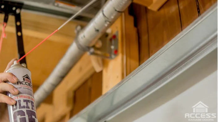 A hand sprays ACCESS GARAGE DOORS ULTRA LUBE into a garage door track,