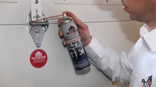 man holding a spray can spraying it on a garage door mechanical piece